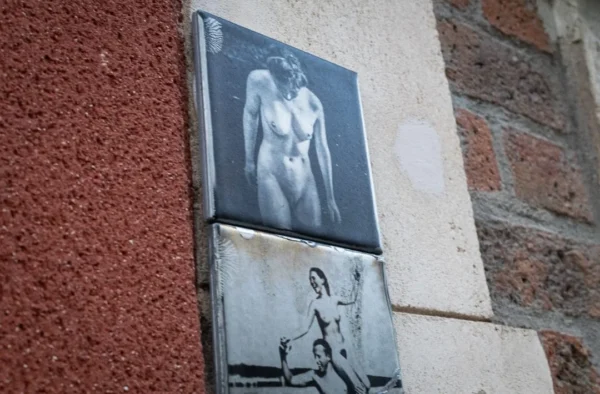 Muriel · 1080 x 710 Cette photographie montre un panneau mural avec deux images superposées. Le sujet principal est une affiche représentant un homme nu en posture dynamique, encadrée par une autre image plus sombre et floue en bas, évoquant un style graffiti ou street art.La composition est verticale, avec un cadrage serré sur le panneau. La lumière semble naturelle, mettant en valeur les contrastes entre les zones claires et sombres. Les couleurs dominantes sont les tons gris, bleu et noir, créant une ambiance urbaine et légèrement mystérieuse. Le style rappelle l’art de rue, avec un côté brut et expressif.