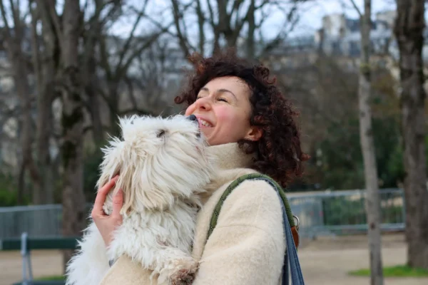 Vera · 6960 x 4640 Cette photographie met en scène une femme comme sujet principal, souriante et tenant un petit chien blanc à poils longs. La composition est simple et centrée, avec un cadrage serré sur les deux sujets.La lumière semble naturelle, douce et légèrement tamisée, créant une ambiance chaleureuse. Les couleurs dominantes sont les tons neutres (beige, gris) et blancs, adoucis par les reflets naturels.Le style est spontané et naturel, évoquant une scène du quotidien. L’ambiance est apaisante et joyeuse, renforcée par le sourire de la femme et l’aspect câlin du chien.