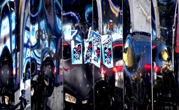 Franck T. · 1400 x 865 Cette photographie capture une scène reflétée dans des miroirs et des surfaces métalliques, créant une composition fragmentée et répétitive. Le sujet principal semble être des éléments urbains, comme des visages et des objets, déformés par les reflets.Le cadrage est serré et dynamique, exploitant les jeux de symétrie et de distorsion. La lumière, bien que tamisée, met en valeur les contrastes entre ombres et éclats lumineux. Les couleurs dominantes sont des teintes froides (bleus, noirs) et des touches chaudes (jaunes, rouges), donnant un style visuel futuriste et onirique. L’ambiance est à la fois mystérieuse et intense, évoquant une atmosphère urbaine et artistique.