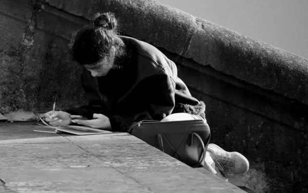 Franck T. · 1400 x 879 Cette photographie en noir et blanc met en scène une personne comme sujet principal, accroupie et concentrée sur une activité manuelle, probablement liée à l'escalade ou au dessin sur une surface rocheuse.La composition est simple et centrée, avec un cadrage serré qui isole le sujet. La lumière, douce et naturelle, crée des contrastes marqués entre ombres et zones éclairées, accentuant les détails et les textures. L’ambiance est contemplative et intime, évoquant la solitude et la concentration. Le style est documentaire et réaliste, renforcé par l'absence de couleurs.