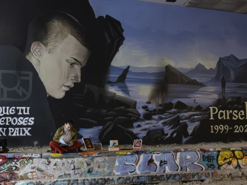 Petit-Montrouge Cette photographie montre un mural urbain avec pour sujet principal un homme en silhouette, entouré d'éléments évoquant un paysage post-apocalyptique. Le cadrage est serré sur le visage et la scène derrière lui, avec des inscriptions en espagnol ("Que tu retoses en paix" et "Parsek 1999-2021").La lumière semble artificielle, mettant en valeur les contrastes. Les couleurs dominantes sont des tons sombres (bleus, noirs) avec des touches de rouge et de blanc pour les graffitis. Le style est street art, réaliste et expressif, créant une ambiance mélancolique et engagée.