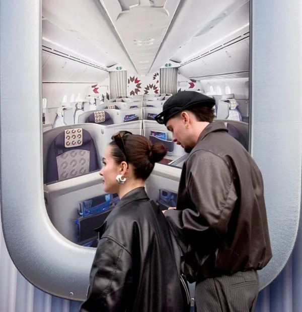 Pascale CHESNOT · 07/03/2026 · 969 x 1000 Cette photographie montre deux personnes à bord d'un avion, probablement des membres d'équipage. Le sujet principal est leur interaction près d'une porte ou d'un hublot.La composition met en valeur l'intérieur de l'avion avec des rangées de sièges et des passagers assoupis. Le cadrage est serré sur les deux individus, avec une profondeur de champ qui inclut l'habitacle en arrière-plan.La lumière est douce et artificielle, typique d'un éclairage intérieur. Les couleurs dominantes sont les tons neutres (gris, beige) avec des touches de bleu et de rouge (sièges et hublots).L'ambiance est calme et professionnelle, évoquant un moment de routine en vol.