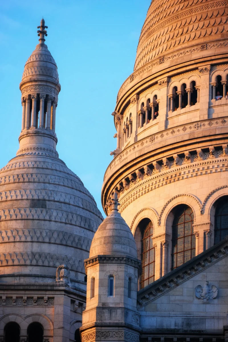 Denis · 21/03/2026 · 3265 x 4898 Cette photographie met en scène la **Sacré-Cœur de Montmartre**, avec ses **dômes blancs** comme sujet principal. La composition joue sur les **courbes architecturales** et les jeux d’ombres. Le cadrage serré isole les dômes, créant une perspective dynamique.La lumière, douce et dorée, suggère un **coup de soleil** en fin de journée, adoucissant les contours. Les **couleurs dominantes** sont des tons **beiges et blancs**, rehaussés par le bleu profond du ciel.Le style est **classique et monumental**, évoquant une ambiance **sereine et spirituelle**, typique des lieux emblématiques de Paris.