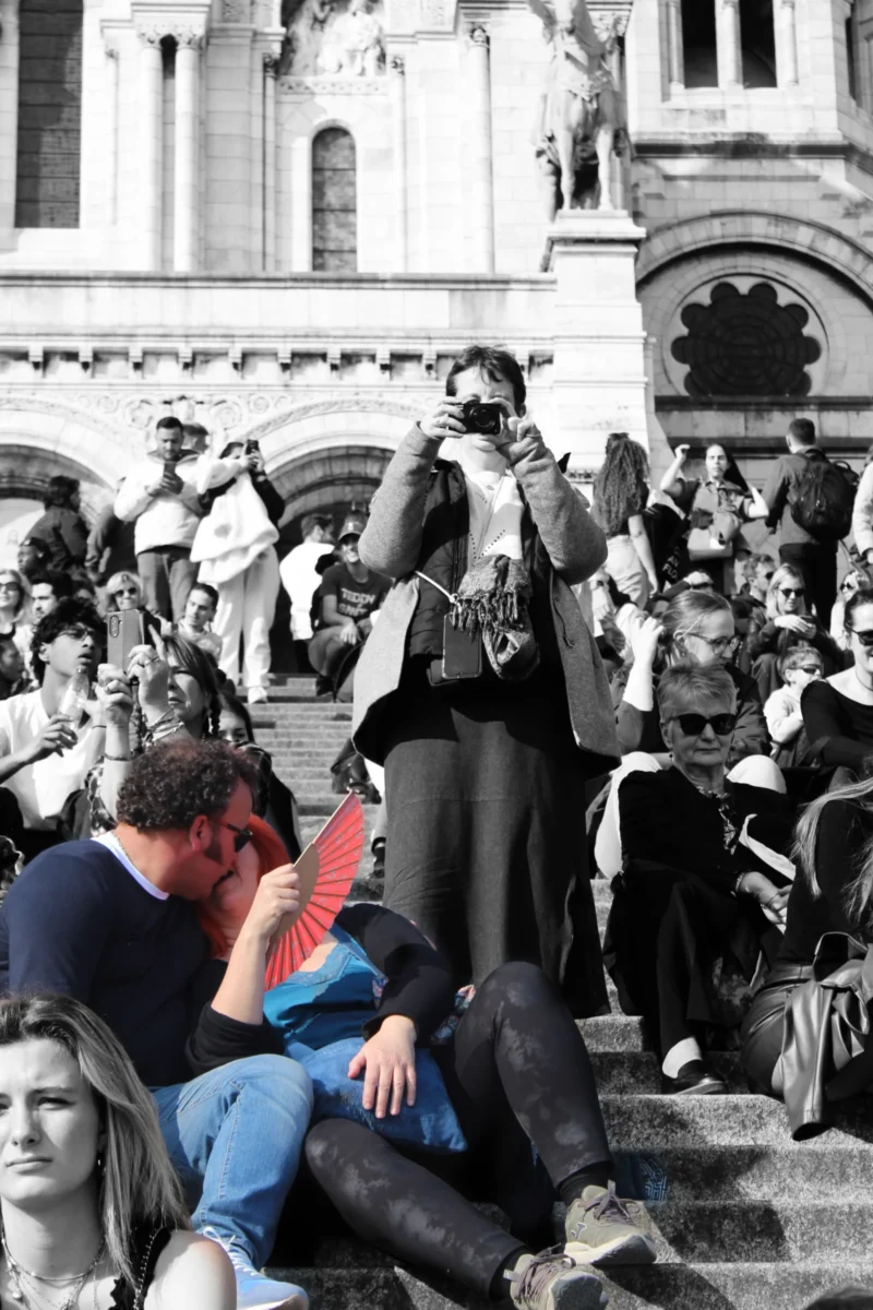 Vartika · 18/02/2026 · 3456 x 5184 Cette photographie montre une scène urbaine animée. Le sujet principal semble être un homme assis par terre, en train de manger un sandwich, tandis qu'autour de lui, des personnes sont assises ou debout sur des marches.La composition est dynamique, avec un cadrage serré sur les individus. La lumière est naturelle, mais contrastée, créant des ombres marquées. Les couleurs dominantes sont des tons gris et sépia, donnant un aspect vintage à l'image.L'ambiance est celle d'une foule en mouvement, dans un lieu public, probablement un monument ou une place emblématique. Le style est documentaire et spontané.