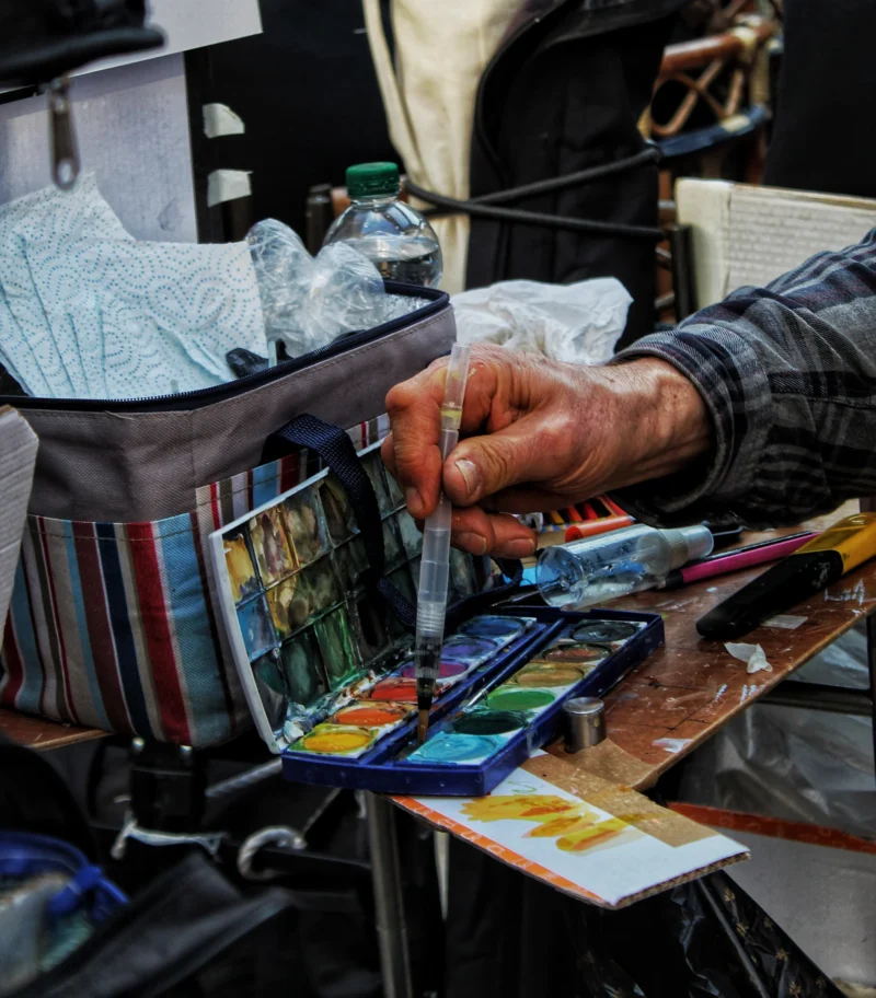 Vartika · 18/02/2026 · 3456 x 3938 Cette photographie montre une personne manipulant des cartes illustrées, probablement des cartes à collectionner ou des œuvres artistiques. Le sujet principal est les mains et les cartes, disposées sur une table.La composition est serrée, centrée sur les détails des cartes et des objets. Le cadrage est rapproché, mettant en valeur les textures et couleurs. La lumière semble naturelle, douce et légèrement tamisée, créant des ombres douces.Les couleurs dominantes sont vives et variées, avec des teintes chaudes et froides. L’ambiance est artisanale et studieuse, évoquant un marché ou une exposition d’art. Le style est réaliste et documentaire.