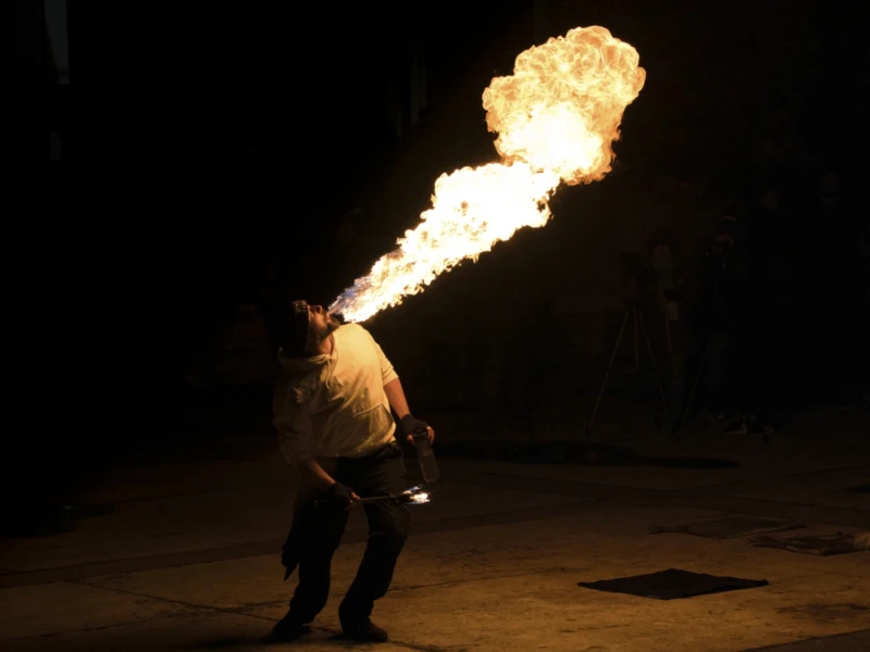 Un artiste crache un jet de feu enflammé dans une ambiance nocturne, spectacle pyrotechnique en extérieur.