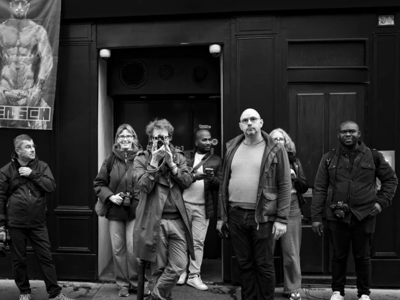Ahmet, Muriel, Thomas, Don, Thibault, AnJo et Terry de Photos in Paris Six personnes posant devant une entrée de bâtiment avec une affiche publicitaire, certaines tenant des appareils photo