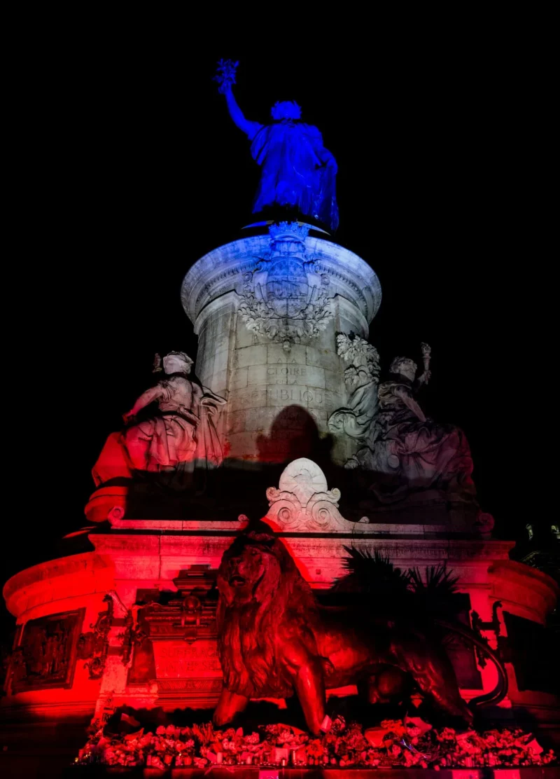 Pascal SC · 13/11/2025 · 1381 x 1920 Cette photographie met en scène une statue monumentale éclairée de nuit. Le sujet principal est une figure debout sur un piédestal, entourée de personnages allégoriques.La composition est symétrique, avec un cadrage serré sur la statue. Les lumières colorées, principalement bleues et rouges, créent un contraste saisissant. Les couleurs dominantes sont le bleu et le rouge, donnant une ambiance dramatique et solennelle.Le style est épuré, axé sur l'effet lumineux et l'atmosphère nocturne, évoquant une scène presque mystique et puissante.