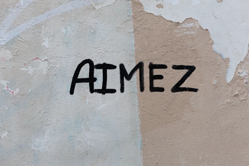 Claude · 5675 x 3783 Cette photographie montre principalement un graffiti écrit en lettres manuscrites noires sur un mur abîmé. Le mot "AIMEZ" est le sujet central. La composition est simple, avec un cadrage serré sur le texte et une partie du mur dégradé, séparé par une ligne diagonale.Les couleurs dominantes sont les tons beiges et blancs du mur, contrastant avec le noir du graffiti. La lumière semble naturelle, mettant en valeur les textures et les dégradations du mur. Le style est brut et spontané, évoquant une ambiance urbaine et authentique.