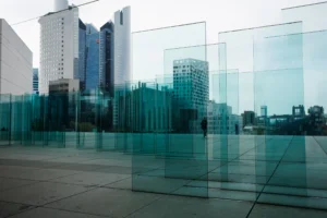Claude · 5842 x 3895 Cette photographie met en scène une **architecture moderne** avec un **miroir d'eau** reflétant des gratte-ciels. Le **sujet principal** est la symétrie entre les bâtiments et leur reflet, créant une illusion de continuité.La **composition** est épurée, avec un **cadrage horizontal** large. La **lumière** est douce, légèrement bleutée, suggérant un jour couvert ou une ambiance matinale. Les **couleurs dominantes** sont les tons gris-bleutés et verts, renforçant une atmosphère **minérale et apaisante**.Le **style** est contemporain, presque abstrait, évoquant une **ambiance urbaine et onirique**.