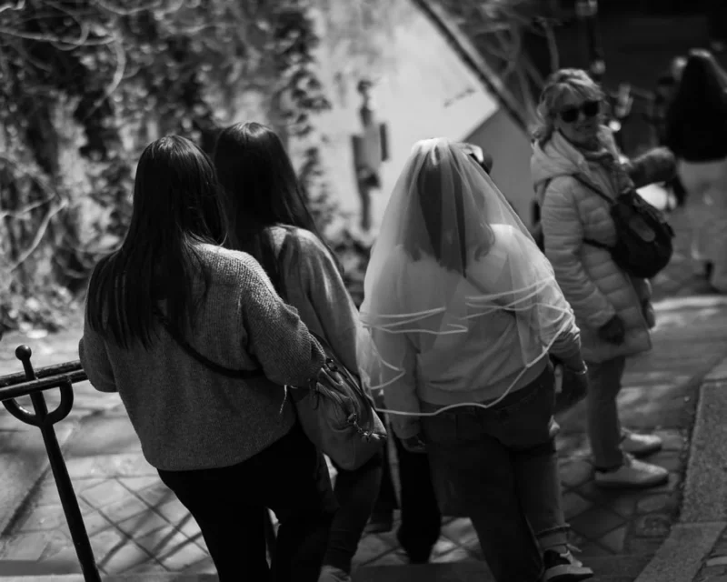 Laurence · 21/03/2026 · 1125 x 900 Cette photographie en noir et blanc capture un moment émotionnel entre trois personnes. Le sujet principal semble être une femme en hijab, entourée et soutenue par deux autres femmes, dont l’une la console en l’enlaçant.La composition est serrée, centrée sur l’interaction humaine. Le cadrage est rapproché, mettant l’accent sur les visages et les gestes. La lumière est douce et naturelle, créant des contrastes subtils.L’ambiance est intime et touchante, renforcée par le monochrome qui accentue les émotions. Le style est documentaire et réaliste, évoquant une scène de vie authentique et poignante.