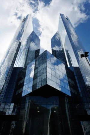 Claude · 3771 x 5657 Cette photographie met en scène un **gratte-ciel moderne** aux formes géométriques anguleuses et à la façade en verre. Le **sujet principal** est l’architecture futuriste, reflétant le ciel bleu et les nuages.La **composition** est centrée, avec un **cadrage serré** mettant en valeur les lignes verticales et les jeux de lumière. La **lumière**, naturelle et vive, accentue les reflets et les contrastes. Les **couleurs dominantes** sont le bleu du ciel, le gris des structures métalliques et le noir des ombres.Le style est **urbain et contemporain**, évoquant une ambiance **dynamique et sophistiquée**, typique des métropoles modernes.