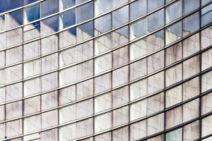 Yvon · 28/03/2026 · 3200 x 2133 Cette photographie met en scène la façade d’un bâtiment moderne en verre et métal. Le sujet principal est la répétition géométrique des panneaux de verre rectangulaires, reflétant partiellement le ciel.La composition est épurée et symétrique, avec un cadrage serré qui accentue les lignes verticales et horizontales. La lumière naturelle, douce et diffuse, adoucit les contrastes. Les couleurs dominantes sont des teintes neutres : gris clair, blanc et bleu pâle des reflets.Le style architectural est contemporain et minimaliste, évoquant une ambiance froide et sophistiquée, presque abstraite.