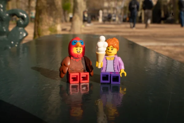 Juan MEDINA MARTINEZ · 6865 x 4579 Cette photographie met en scène deux figurines Lego posées sur une surface réfléchissante, probablement de l’eau. Le sujet principal est ces deux personnages stylisés, l’un masculin avec une barbe et un chapeau rouge, l’autre féminin en tenue pourpre.La composition est symétrique et minimaliste, avec un cadrage serré. La lumière naturelle éclaire les figurines, créant des ombres nettes et des reflets. Les couleurs dominantes sont les tons vifs des Lego (rouge, violet, blanc) contrastant avec le noir de la surface.Le style est épuré et ludique, évoquant une ambiance à la fois joyeuse et légèrement surréaliste.
