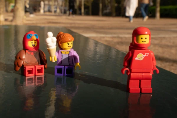 Juan MEDINA MARTINEZ · 6865 x 4579 Cette photographie montre trois figurines Lego disposées sur une surface réfléchissante, probablement de l’eau.**Sujet principal** : Les figurines Lego, habillées et accessoirisées.
**Composition** : Alignement en triangle, avec une symétrie partielle.
**Cadrage** : Gros plan, centré sur les figurines.
**Lumière** : Naturelle, douce, avec des ombres légères.
**Couleurs dominantes** : Rouge, violet, bleu, blanc et noir.
**Style** : Ludique et minimaliste.
**Ambiance** : Joyeuse et créative, renforcée par le reflet et la simplicité du décor.