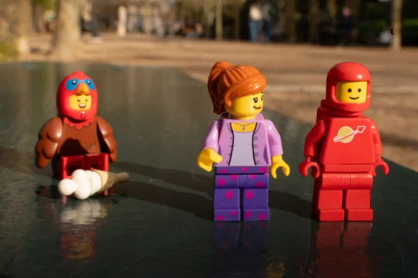 Juan MEDINA MARTINEZ · 6865 x 4579 Cette photographie montre trois figurines Lego posées près d’une surface réfléchissante, probablement de l’eau. Le sujet principal est ces figurines, habillées de manière variée : une en tenue de bain, une autre en vêtements violets, et la dernière en combinaison rouge.La composition est symétrique et linéaire, avec un cadrage serré. La lumière naturelle éclaire les figurines, créant des ombres douces. Les couleurs dominantes sont vives : rouge, violet et bleu, avec des touches de blanc et de noir. Le style est ludique et minimaliste, évoquant une ambiance joyeuse et créative.