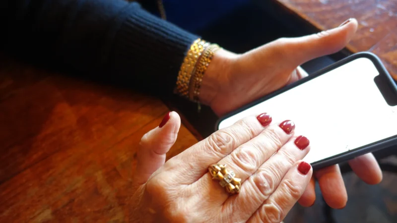 Pierre · 21/02/2026 · 5472 x 3080 Cette photographie met en scène une main tenant un smartphone. Le sujet principal est les doigts manucurés, avec des ongles rouges, et les bijoux (bracelets et bague).La composition est serrée, centrée sur les mains et l’appareil. Le cadrage est rapproché, excluant l’arrière-plan. La lumière est douce et naturelle, éclairant les détails des mains et du téléphone. Les couleurs dominantes sont les tons chauds (peau, bois) et les rouges vifs des ongles.Le style est simple et réaliste, avec une ambiance intime et quotidienne.