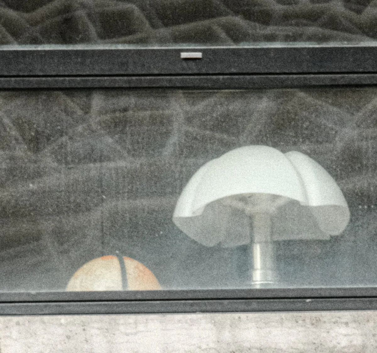 Nathalie F. · 21/02/2026 · 2276 x 2128 Cette photographie montre un **parapluie blanc** reflété sur une vitre, sujet principal flou. Le cadrage est serré, centré sur la surface vitrée et partiellement sur un mur texturé en arrière-plan.La lumière semble naturelle, tamisée, créant des reflets et des contrastes doux. Les couleurs dominantes sont les tons gris (mur) et blanc (parapluie), avec une touche de beige. Le style est réaliste et minimaliste, évoquant une ambiance calme et légèrement mélancolique, presque abstraite grâce aux reflets.