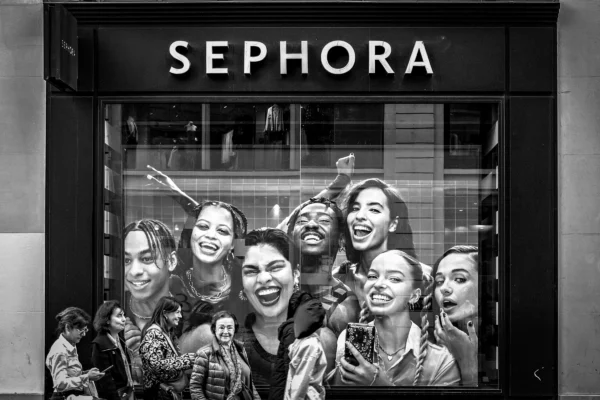 AnJo Beckers · 07/03/2026 · 4729 x 3153 Cette photographie montre une vitrine de magasin **Sephora** avec une affiche publicitaire en noir et blanc. Le **sujet principal** est un groupe de femmes souriantes, posant joyeusement. La **composition** est dynamique, avec un cadrage serré sur les visages, créant une ambiance conviviale. La **lumière** est douce, mettant en valeur les traits des modèles. Les **couleurs dominantes** sont les nuances de gris, renforçant l’aspect moderne et élégant. Le **style** est épuré et professionnel, évoquant une **ambiance** positive et inclusive, typique des campagnes marketing de beauté.