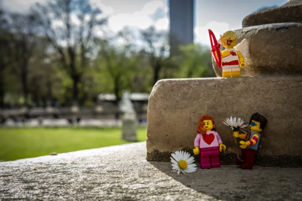 AnJo Beckers · 14/03/2026 · 4811 x 3207 Cette photographie met en scène des figurines Lego posées sur un tombereau en pierre, dans un cimetière.**Sujet principal** : Les figurines Lego, dont une en tenue de marin et une autre avec une fleur.**Composition** : Cadrage serré sur les figurines, avec un arrière-plan flou de tombes et d'arbres.
**Lumière** : Naturelle et douce, créant des ombres légères.
**Couleurs dominantes** : Verts (végétation), gris (pierres), couleurs vives des Lego (jaune, bleu, rose).
**Style** : Photographie artistique et poétique, mêlant humour et mélancolie.
**Ambiance** : Onirique et contrastée, entre légèreté ludique et gravité du lieu.