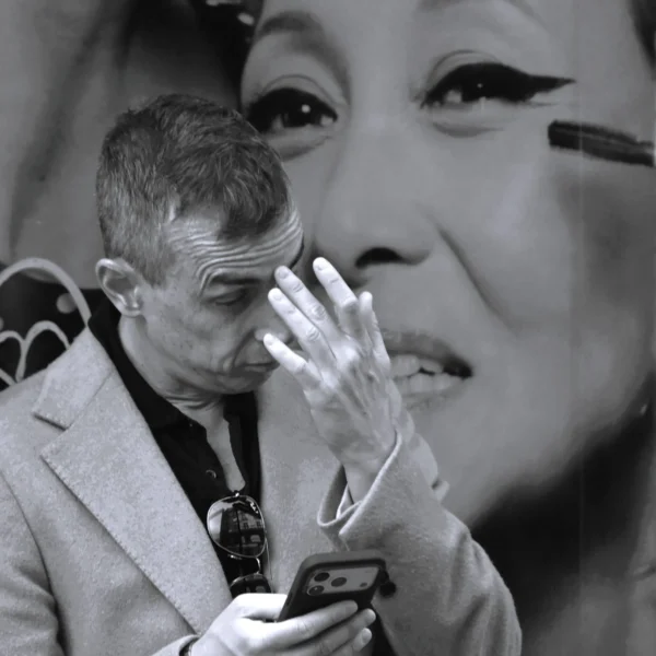 Pierre · 2272 x 2272 Cette photographie en noir et blanc met en scène un homme comme sujet principal, absorbé par son smartphone. La composition joue sur la superposition d’une affiche géante représentant un visage féminin derrière lui, créant un contraste entre intimité et publicité.Le cadrage serré isole l’homme, tandis que l’arrière-plan flou accentue son immersion. La lumière, douce et contrastée, souligne les traits et les textures des vêtements. Les tons gris dominent, renforçant l’ambiance moderne et mélancolique. Le style, sobre et urbain, évoque une réflexion sur la connexion numérique et la solitude dans l’espace public.