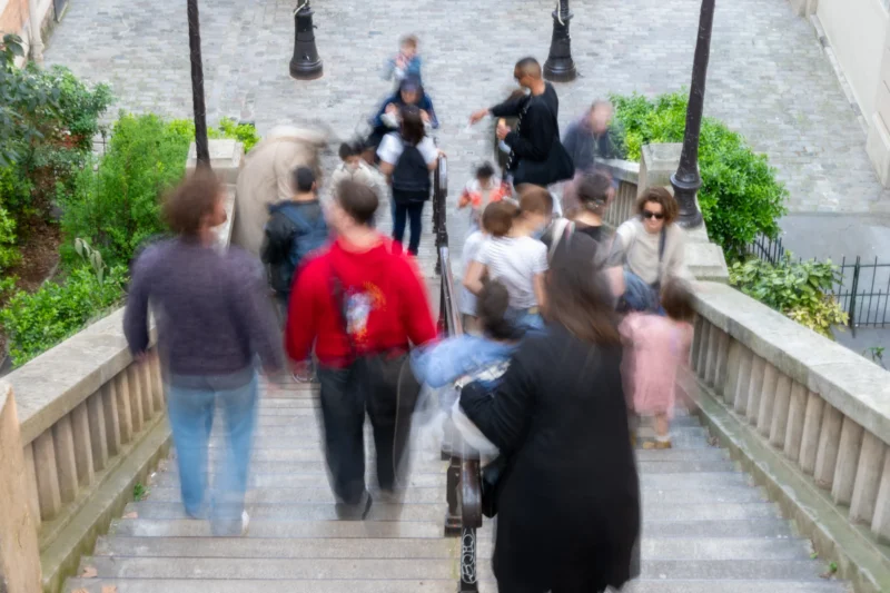 Jean-Marc · 21/03/2026 · 5312 x 3541 Cette photographie montre un groupe de personnes descendant ou montant un escalier extérieur en pierre. Le sujet principal est l’interaction sociale entre les individus.La composition est dynamique, avec un cadrage légèrement flou qui met en valeur les mouvements. La lumière semble naturelle, probablement en journée, avec des ombres douces. Les couleurs dominantes sont des tons neutres (gris, beige) et quelques touches de rouge et vert.Le style est documentaire et spontané, capturant une scène de vie quotidienne. L’ambiance est conviviale et légèrement animée, reflétant une activité collective en extérieur.