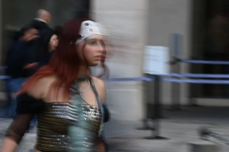 Pierre · 08/11/2025 · 3808 x 2533 Cette photographie met en scène une personne vêtue d’un costume cosplay, probablement inspiré d’un personnage de science-fiction ou de fantasy. Le sujet principal est flou, suggérant un mouvement rapide.La composition est dynamique, avec un cadrage serré sur le personnage en mouvement devant une barrière bleue. La lumière semble naturelle mais tamisée, créant des contrastes doux. Les couleurs dominantes sont les teintes vertes métallisées du costume, rehaussées par des touches de rouge dans les cheveux.L’ambiance est festive et légèrement floue, évoquant un événement public comme une convention. Le style est réaliste et spontané.