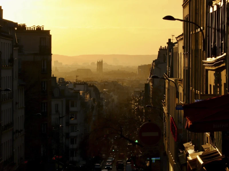 De Belleville à Ménilmontant Cette photographie capture une ville en contrebas lors d’un coucher de soleil. Le sujet principal est une rue étroite bordée de bâtiments anciens, avec une perspective descendante.La composition joue sur les lignes architecturales et la profondeur. Le cadrage est serré, mettant en valeur les détails des façades et des balcons. La lumière dorée et tamisée crée une ambiance chaleureuse et nostalgique. Les couleurs dominantes sont les tons chauds (oranges, jaunes) contrastant avec les ombres sombres.Le style est réaliste et légèrement dramatique, évoquant une atmosphère mélancolique et poétique.