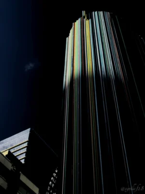 Cyrille · 28/03/2026 · 1519 x 2026 Cette photographie met en scène un **gratte-ciel moderne** comme sujet principal, cadré en contre-plongée. La **composition** verticale accentue sa hauteur, avec des lignes architecturales parallèles qui créent un effet graphique saisissant. La **lumière**, contrastée et dramatique, éclaire partiellement la façade, produisant des jeux d’ombres et de reflets dorés.Les **couleurs dominantes** sont le noir profond du ciel et les teintes grises et jaunes de l’immeuble. Le **style** est épuré, presque abstrait, évoquant une **ambiance nocturne mystérieuse et urbaine**, renforcée par les contrastes lumineux.