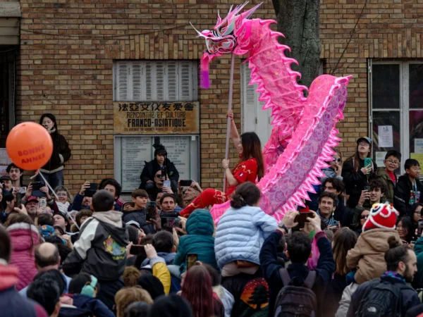 Cyrille · 2026 x 1520 Cette photographie capture une scène festive avec un **dragon gonflable rose** comme sujet principal, porté par des participants. La **composition** montre une foule dense, avec des spectateurs en arrière-plan. Le **cadrage** est serré sur le dragon et les porteurs, créant un effet dynamique.La **lumière** semble naturelle, avec des tons doux. Les **couleurs dominantes** sont le rose vif du dragon, contrastant avec les teintes neutres des vêtements et des bâtiments en arrière-plan. L’ambiance est **joyeuse et animée**, typique d’une célébration culturelle, probablement une fête traditionnelle.