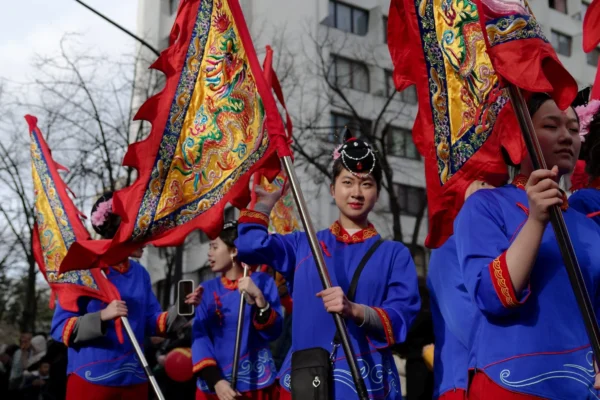 Cyrille · 2026 x 1351 Cette photographie capture un groupe de personnes participant à une procession traditionnelle. Les sujets principaux sont des individus vêtus de costumes bleus ornés, portant des bannières rouges et dorées richement décorées.La composition montre une mise en scène dynamique, avec un cadrage serré sur les participants en mouvement. La lumière semble naturelle, bien que légèrement contrastée, mettant en valeur les couleurs vives. Les couleurs dominantes sont le bleu des vêtements, le rouge et l’or des bannières, créant une ambiance festive et culturelle. Le style évoque une tradition asiatique, renforçant une ambiance solennelle et célébrative.