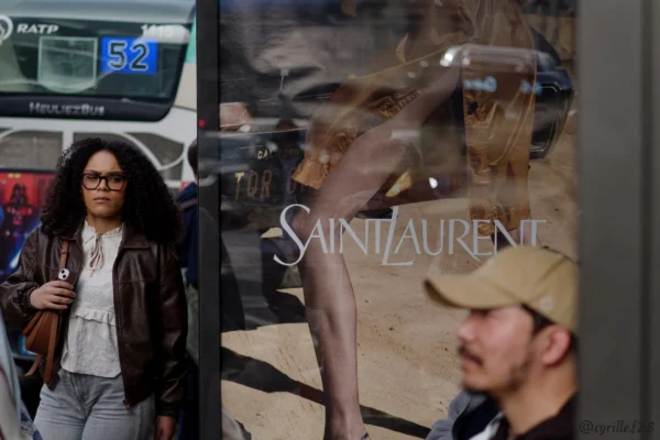 Cyrille GONTIER · 07/03/2025 · 2026 x 1351 Cette photographie montre une vitrine de la marque **Saint Laurent**. Le sujet principal est le reflet d’une silhouette masculine dans la vitrine, ainsi que le logo distinctif de la marque.La composition joue sur les reflets et les contrastes entre l’intérieur et l’extérieur. Le cadrage est serré sur la vitrine, avec une personne floue en premier plan à gauche. La lumière est naturelle et tamisée, créant une ambiance urbaine sophistiquée. Les couleurs dominantes sont neutres (beige, noir) avec des touches de gris et de blanc. Le style est élégant et minimaliste, évoquant un luxe discret. L’ambiance est moderne et chic.
