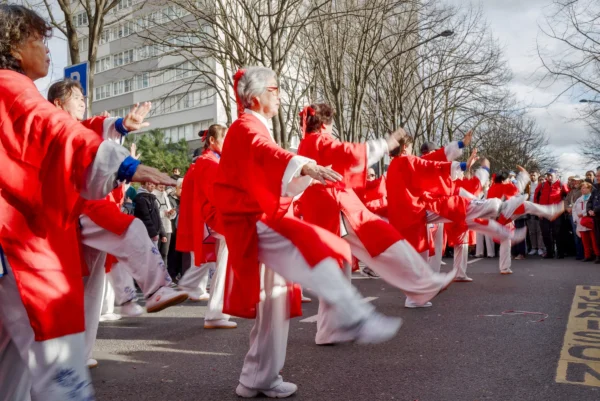 Frédéric · 2517 x 1680 Cette photographie capture un groupe de personnes vêtues de tenues sportives rouges et blanches, probablement en train de pratiquer une activité martiale ou une démonstration collective. Le sujet principal est ce groupe en mouvement synchronisé.La composition montre une perspective dynamique, avec un cadrage serré sur les participants en premier plan et un arrière-plan flou. La lumière semble naturelle, avec une ambiance légèrement brumeuse ou nuageuse. Les couleurs dominantes sont le rouge vif des vêtements et le blanc des accessoires, créant un contraste marqué. Le style est énergique et rythmé, évoquant une ambiance de discipline et de coordination collective.