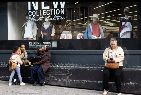 Muriel Juan · 1080 x 727 Cette photographie montre trois personnes devant une affiche publicitaire pour la collection "New Collection Youth Culture" de la marque New Balance.**Sujet principal** : Les trois individus, dont deux semblent discuter et une troisième observe.
**Composition** : Cadrage serré sur les personnes, avec l’affiche en arrière-plan.
**Cadrage** : Plan moyen, mettant en valeur les visages et les interactions.
**Lumière** : Naturelle et légèrement contrastée, avec des ombres marquées.
**Couleurs dominantes** : Teintes neutres (gris, beige) et touches de couleurs vives sur les vêtements des personnes et l’affiche.
**Style** : Photographie documentaire, réaliste.
**Ambiance** : Urbaine et dynamique, avec une touche de modernité.