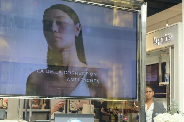 Camilla · 07/03/2026 · 6000 x 4000 Cette photographie montre une affiche publicitaire comme sujet principal. Elle présente un visage masculin stylisé avec un bandeau sur les yeux, évoquant un look futuriste ou technologique. La composition est centrée sur cette affiche, encadrée par des vitrines de magasins.Le cadrage est serré sur l'affiche, avec une personne partiellement visible en bas à droite. La lumière semble artificielle et uniforme, typique d’un éclairage intérieur. Les couleurs dominantes sont des teintes froides (bleus, gris) et des tons neutres.L’ambiance est urbaine et moderne, avec une touche de mystère renforcée par le texte "LA DE LA CORRECTION ANTICHES". Le style est épuré et contemporain.