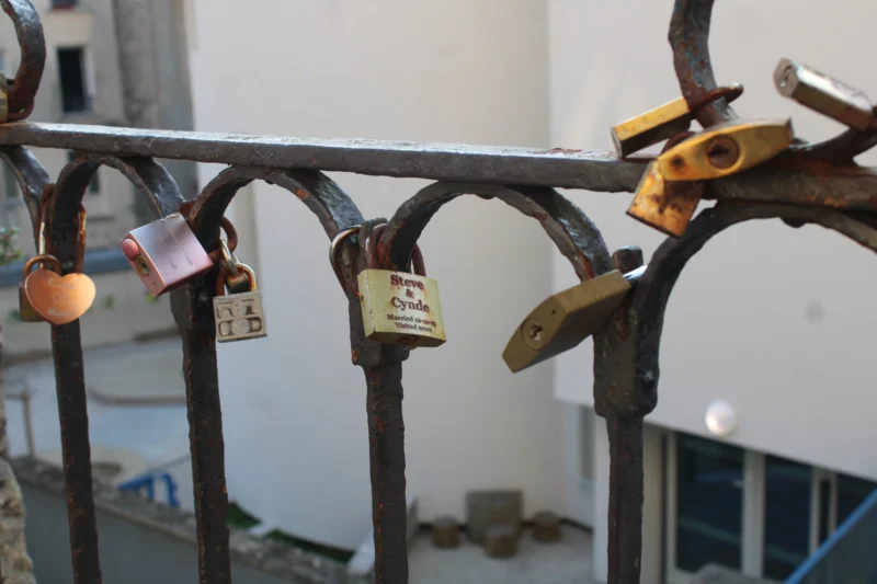 Roberta · 21/03/2026 · 6000 x 4000 Cette photographie montre un ensemble de cadenas accrochés à une structure métallique, probablement une rambarde ou un garde-corps. Le sujet principal est ces cadenas, symboles souvent associés aux serments d’amour ou aux messages.La composition est serrée, avec un cadrage rapproché mettant en valeur les détails des cadenas. La lumière semble naturelle et douce, éclairant les objets sans ombres marquées. Les couleurs dominantes sont neutres (gris, métal) avec quelques touches de couleurs vives sur les cadenas (jaune, orange).Le style est documentaire et réaliste, créant une ambiance à la fois banale et poétique, évoquant la mémoire et les promesses.