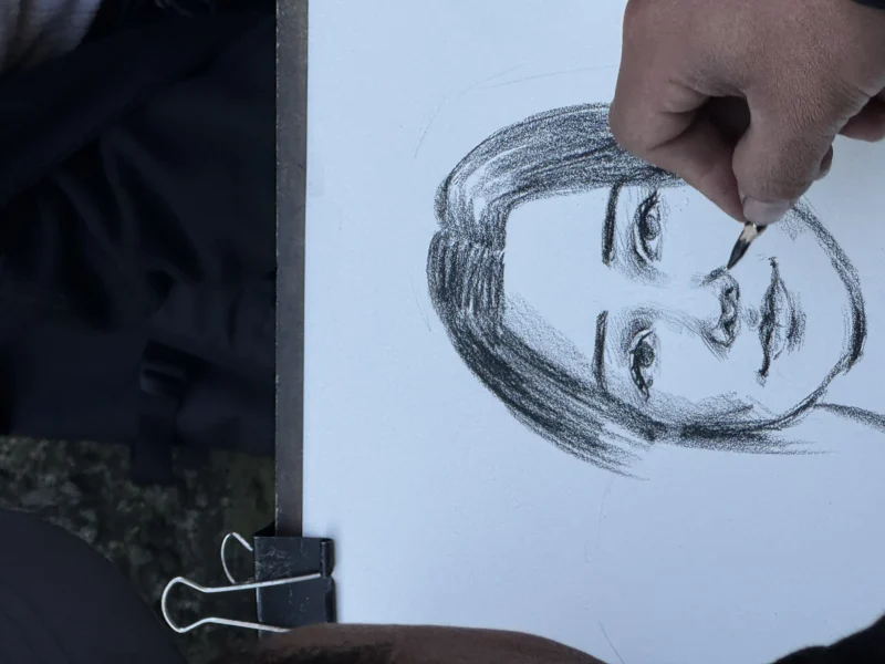 Heike · 21/03/2026 · 4032 x 3024 Cette photographie montre une personne en train de dessiner un portrait au crayon sur une feuille blanche. Le sujet principal est le dessin en cours, représentant un visage féminin stylisé.La composition est simple, avec un cadrage serré sur la main et le papier. La lumière est douce et naturelle, éclairant bien les traits du dessin. Les couleurs dominantes sont les tons gris du crayon et le blanc de la feuille, créant une ambiance sobre et minimaliste. Le style est réaliste mais esquissé, avec des lignes expressives. L'atmosphère est calme et concentrée, reflétant le processus créatif.