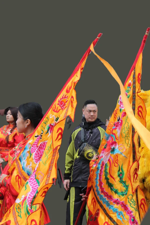 Sophie · 22/07/2025 · 2848 x 4272 Cette photographie met en scène un groupe participant à une parade traditionnelle, probablement asiatique. Le sujet principal est un homme vêtu d’une tenue noire et dorée, entouré de danseurs brandissant de grands éventails colorés.La composition est dynamique, avec un cadrage serré sur les personnages. Les couleurs dominantes sont vives : or, rouge, jaune et vert, créant un contraste saisissant. La lumière semble naturelle et met en valeur les détails des costumes.L’ambiance est festive et culturelle, évoquant une célébration traditionnelle riche en symboles et en énergie. Le style est visiblement traditionnel, mêlant mouvement et esthétique ornementale.