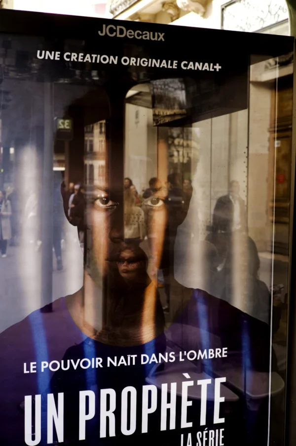 Thomas Ternisien · 07/03/2026 · 2048 x 3080 Cette photographie montre l'affiche d'une série intitulée **« Un Prophète »** (série Canal+).Le sujet principal est un homme au regard intense, vêtu d'un costume sombre, tenant une arme. Le cadrage est serré sur son visage, créant un effet dramatique. L'arrière-plan est sombre et flou, mettant en valeur le personnage.Les couleurs dominantes sont les tons sombres (noirs, gris) avec des éclairages contrastés, renforçant une ambiance tendue et mystérieuse. Le style est réaliste et cinématographique, évoquant une atmosphère de tension et de danger.
