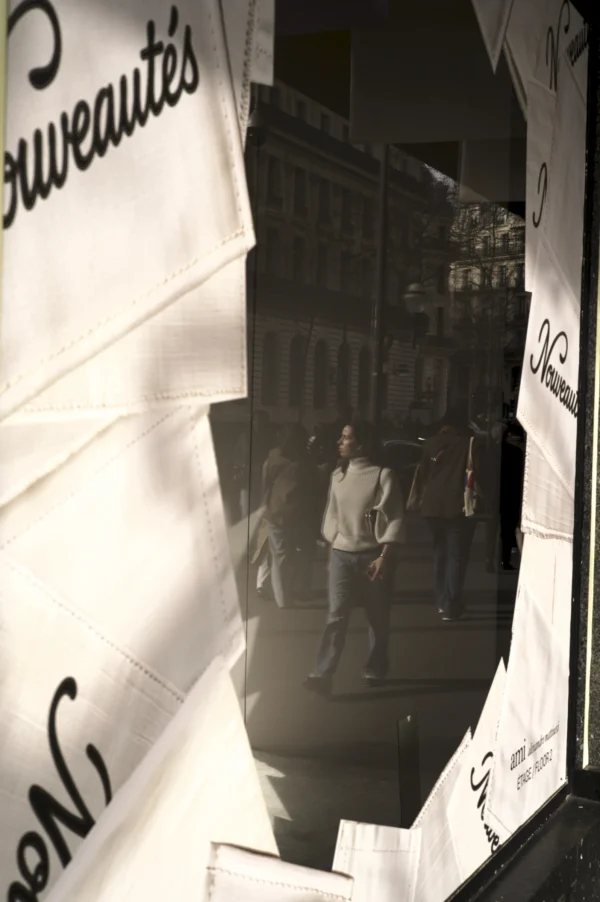 Thomas Ternisien · 07/03/2026 · 2048 x 3080 Cette photographie montre un homme comme sujet principal, reflété dans une vitrine ou un miroir. La composition utilise un cadrage en contre-plongée, accentuant la silhouette. La lumière est tamisée, créant des contrastes doux et des ombres marquées.Les couleurs dominantes sont les tons froids et sombres, avec des touches de gris et de noir. Le style semble documentaire ou urbain, capturant une scène spontanée. L’ambiance est à la fois mystérieuse et réaliste, évoquant une rue nocturne ou peu éclairée.