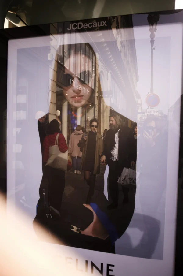 Thomas Ternisien · 07/03/2026 · 2048 x 3080 Cette photographie présente une affiche publicitaire pour la marque **JC Decaux**.Le **sujet principal** est une silhouette féminine stylisée, vêtue d’une tenue sombre avec des détails colorés (rouge, bleu). Elle tient un accessoire et semble en mouvement. La **composition** est épurée, avec un fond clair et des éléments graphiques minimalistes. Le **cadrage** est serré, mettant en valeur la silhouette.Les **couleurs dominantes** sont le noir, gris et touches de rouge/bleu. La **lumière** est douce et uniforme, créant un effet moderne et épuré. Le **style** est contemporain, presque abstrait, évoquant une **ambiance** urbaine et dynamique.