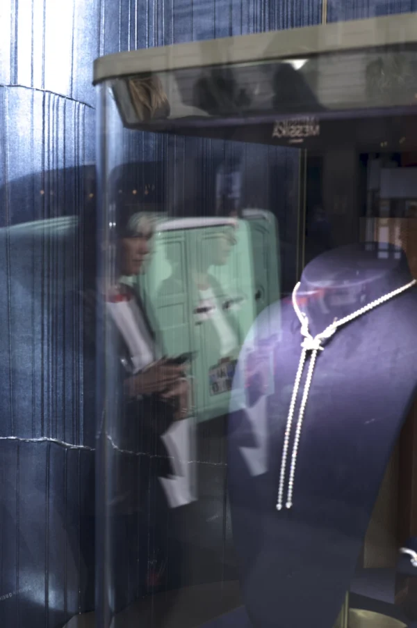 Thomas Ternisien · 07/03/2026 · 2048 x 3080 Cette photographie montre un reflet dans une vitre, capturant deux personnes à l'intérieur d'un espace confiné, probablement un ascenseur.Le sujet principal semble être le reflet flou et légèrement surexposé d'un individu en tenue blanche et d'un autre en noir. La composition est symétrique, centrée sur la vitre. Le cadrage est serré, limitant le champ de vision.Les couleurs dominantes sont des tons froids (gris, bleu) et des reflets blancs. La lumière est diffuse, créant une ambiance mystérieuse et légèrement floue. Le style est documentaire et spontané, évoquant une sensation d'attente ou de mouvement.