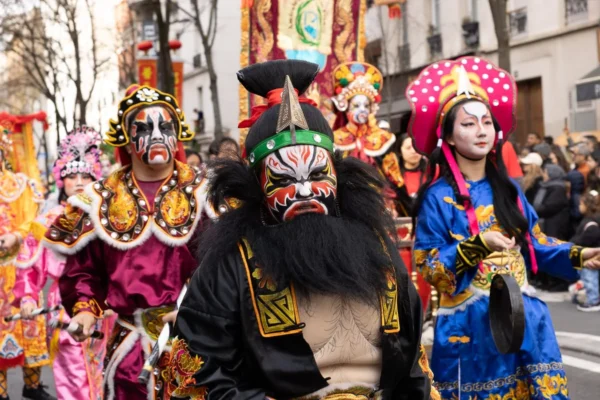 Laurence · 1350 x 900 Cette photographie capture une scène de défilé traditionnel riche en couleurs. Le sujet principal est un groupe de participants vêtus de costumes extravagants, inspirés de styles asiatiques, avec des masques et des parures ornées. La composition montre plusieurs personnages en premier plan, avec des détails complexes comme des plumes, des broderies et des accessoires brillants.Le cadrage est serré, mettant en valeur les visages et les costumes. La lumière semble naturelle, bien répartie, mettant en relief les couleurs vives. Les teintes dominantes sont le rouge, le bleu, l’or et le noir, créant une ambiance festive et mystique. Le style évoque une célébration culturelle, pleine d’énergie et de tradition.