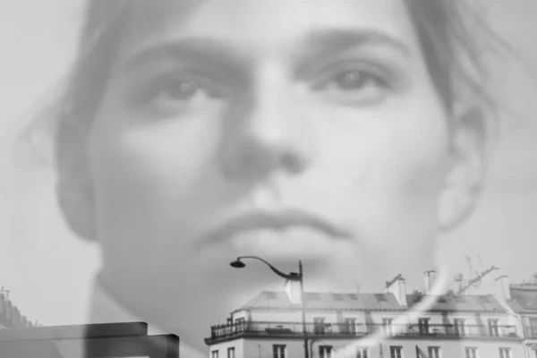 Laurence Givry · 07/03/2026 · 1350 x 900 Cette photographie présente une femme en gros plan comme sujet principal, avec un cadrage serré sur son visage. En arrière-plan flou, on distingue une ville en noir et blanc, partiellement intégrée dans son profil.La lumière semble douce et uniforme, sans contrastes marqués. Les couleurs dominantes sont les tons gris et blancs, avec une touche de bleu froid. Le style est artistique et onirique, mêlant réalisme et abstraction. L’ambiance est à la fois introspective et mystérieuse, évoquant une fusion entre le sujet et son environnement urbain.