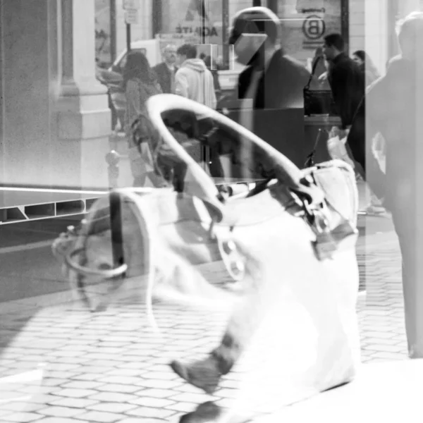 Laurence Givry · 07/03/2026 · 900 x 900 Cette photographie en noir et blanc capture une scène urbaine dynamique. Le sujet principal est un enfant en mouvement, esquivant un vélo renversé, vêtu d’un long manteau clair. La composition est déséquilibrée, avec un cadrage serré sur l’enfant, créant un effet de flou artistique.Les passants en arrière-plan, floutés, renforcent le sentiment de vitesse. La lumière semble naturelle, avec des contrastes marqués. Les couleurs dominantes, bien que monochromes, jouent sur les nuances de gris et de blanc. Le style est spontané et documentaire, évoquant une ambiance de vie trépidante et imprévisible dans un cadre urbain.