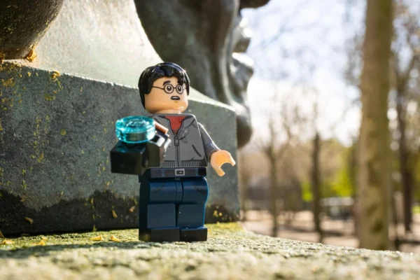 Laurence Givry · 14/03/2026 · 1350 x 900 Cette photographie met en scène une figurine LEGO représentant un personnage en costume, tenant un objet bleu. Le sujet principal est mis en avant devant une statue monumentale en arrière-plan.La composition joue sur le contraste entre le petit format de la figurine et l'imposante statue. Le cadrage est serré sur la figurine, avec un arrière-plan légèrement flou. La lumière est naturelle et douce, créant des ombres douces. Les couleurs dominantes sont les tons gris et bleus, avec des touches de vert en arrière-plan.Le style est réaliste et photographique, évoquant une ambiance à la fois ludique et artistique.