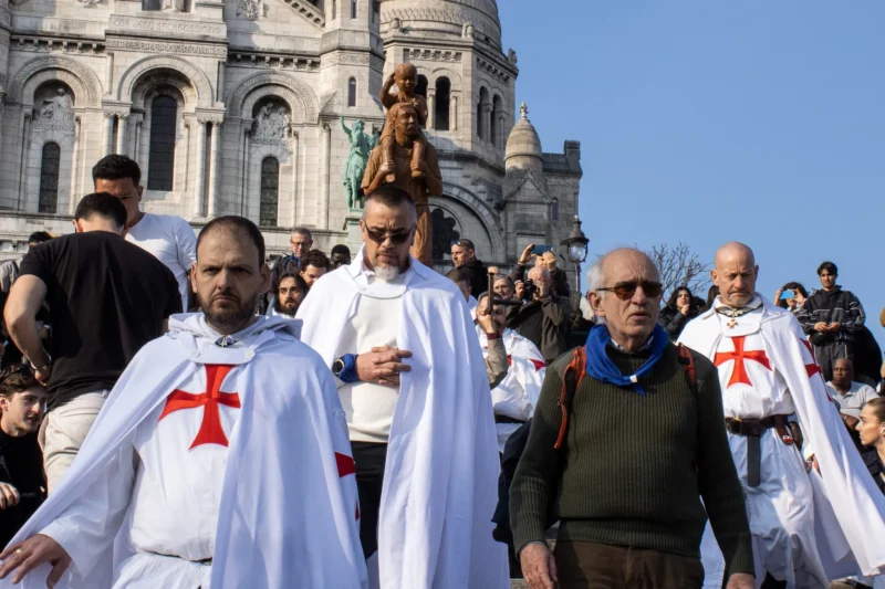 Loubna · 2048 x 1365 Cette photographie montre une procession religieuse devant la basilique du Sacré-Cœur à Paris. Le sujet principal est un groupe de participants vêtus de robes blanches avec des croix rouges, marchant en procession. La composition est dynamique, avec un cadrage serré sur les participants en premier plan et la basilique en arrière-plan. La lumière est naturelle et éclatante, suggérant un jour ensoleillé. Les couleurs dominantes sont le blanc des robes, le rouge des croix, et les tons bleus et gris de la basilique. L’ambiance est solennelle et spirituelle, renforcée par la présence des participants engagés dans une démarche religieuse.