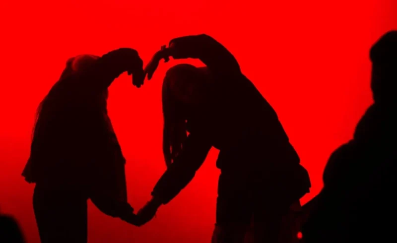 Pascale · 25/12/2025 · 1000 x 612 Cette photographie met en scène deux silhouettes formant un cœur avec leurs mains. Le sujet principal est cette interaction symbolique, évoquant l’amour ou l’affection. La composition est épurée, centrée sur ce geste.Le cadrage est serré, isolant les mains et les bras des corps. La lumière est douce mais contrastée, créant des ombres nettes sur un fond rouge uniforme. Les couleurs dominantes sont le rouge intense et le noir des silhouettes, renforçant l’émotion.Le style est minimaliste et poétique, tandis que l’ambiance est à la fois romantique et mystérieuse.