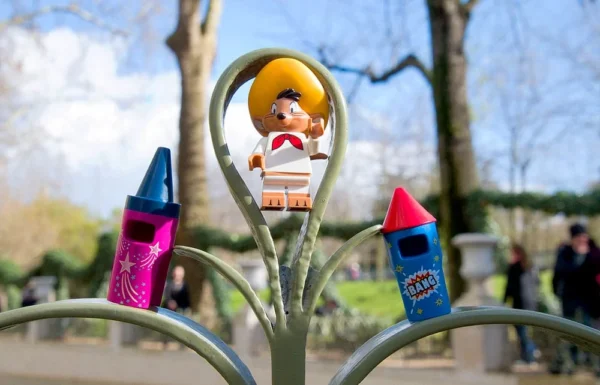Pascale CHESNOT · 14/03/2026 · 1000 x 642 Cette photographie met en scène un **parcmètre décoré** comme une figure de Lego, sujet principal. La composition joue sur l’absurdité humoristique en associant un objet urbain à un jouet enfantin.Le cadrage serré isole le parcemètre, avec des crayons colorés en arrière-plan, ajoutant une touche ludique. La lumière naturelle, douce et légèrement contrastée, éclaire la scène, mettant en valeur les détails.Les **couleurs dominantes** sont vives (bleu, orange, vert) et contrastées, créant une ambiance joyeuse et fantaisiste. Le style est **détourné et créatif**, évoquant une touche d’art urbain ou de street art. L’ambiance est à la fois **poétique et ironique**.
