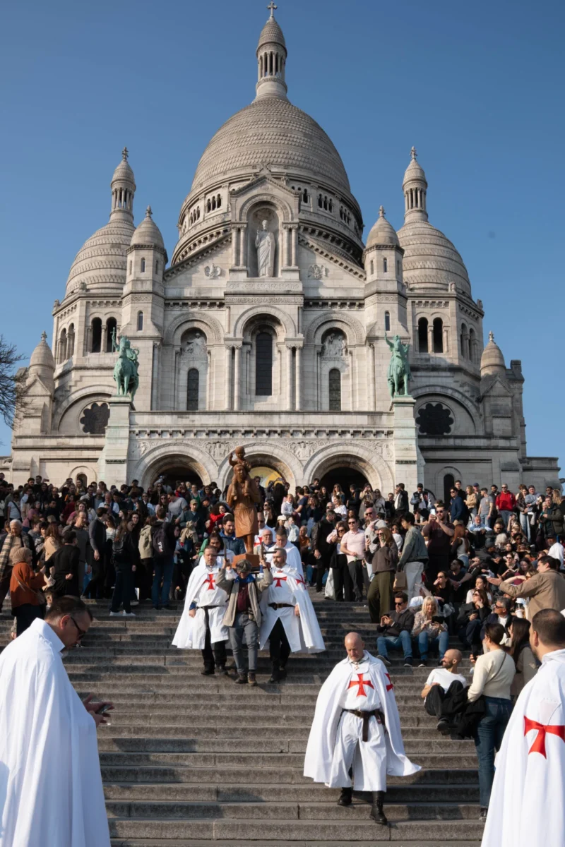 Alice · 21/03/2026 · 3189 x 4784 Cette photographie montre la **Sagrada Família de Barcelone** (en réalité, il s'agit du **Sacré-Cœur de Montmartre à Paris**).Le **sujet principal** est l'imposante basilique blanche avec ses arcs et ses dômes. En premier plan, une **procession religieuse** attire l'attention, avec des participants en robes blanches et capes.La **composition** est dynamique, avec un cadrage serré sur les marcheurs et l'édifice en arrière-plan. La **lumière** est naturelle et claire, créant des contrastes nets. Les **couleurs dominantes** sont les blancs de la basilique et des robes, avec des tons bleutés du ciel.L'**ambiance** est solennelle et spirituelle, renforcée par la foule et l'architecture majestueuse.